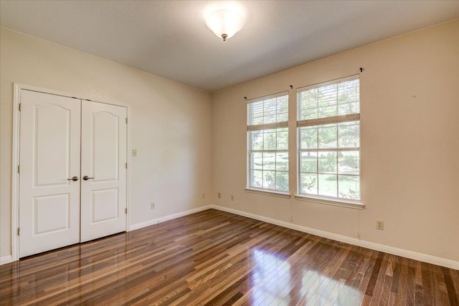 Bedroom 2 on main floor features hardwood floors, access to a full bathroom, and views of the towering oaks. | Image 17