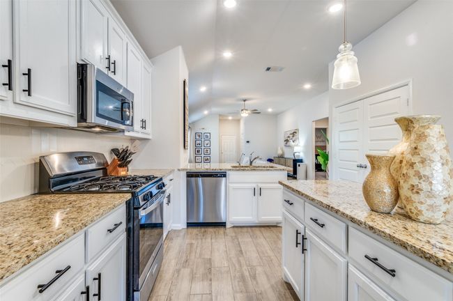 Kitchen featuring a peninsula, white cabinetry, stainless steel appliances, light wood finished floors, and a sink | Image 8