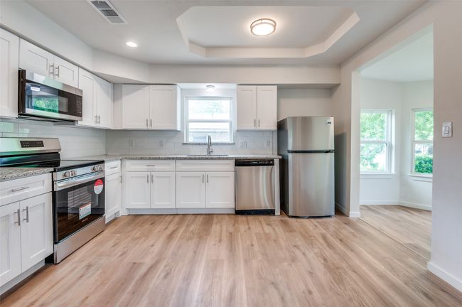 Kitchen featuring tasteful backsplash, visible vents, appliances with stainless steel finishes, and light wood-style flooring | Image 9