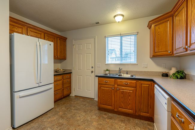 Kitchen featuring a textured ceiling, visible vents, white appliances, brown cabinets, and a sink | Image 10