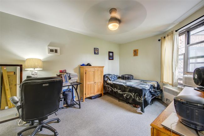 Bedroom featuring radiator heating unit, carpet, an office area, ceiling fan, and cooling unit | Image 4