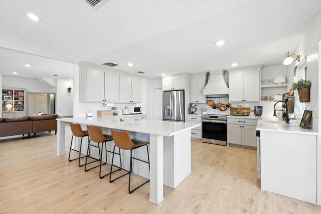 Kitchen with a peninsula, appliances with stainless steel finishes, custom range hood, a breakfast bar area, and light countertops | Image 10
