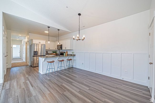 Kitchen with a notable chandelier, light wood-type flooring, a peninsula, white cabinetry, and appliances with stainless steel finishes | Image 5