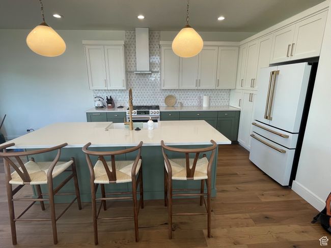 Kitchen with high end white refrigerator, dark wood-type flooring, wall chimney exhaust hood, backsplash, and light countertops | Image 7