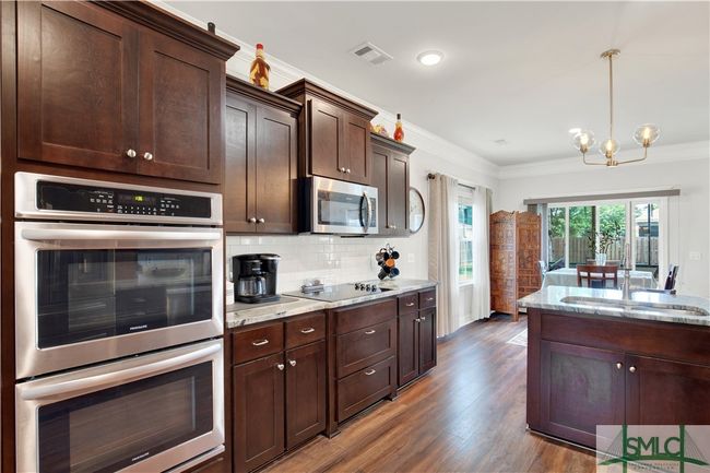 Upgraded cabinetry, double ovens, separate cooktop, granite countertops, tile backsplash, built-in microwave, snack bar with custom lighting | Image 12