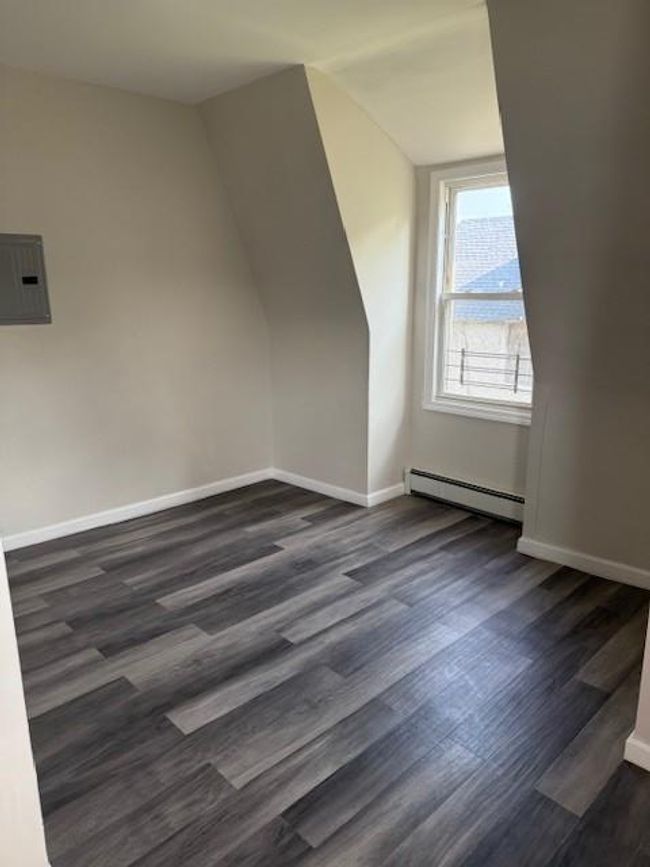 Additional living space with a baseboard radiator, dark wood-type flooring, electric panel, and vaulted ceiling | Image 8