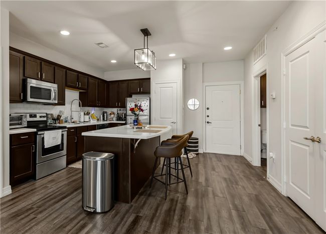 Kitchen featuring stainless steel appliances, dark hardwood / wood-style floors, dark brown cabinetry, a kitchen island, and decorative light fixtures | Image 13