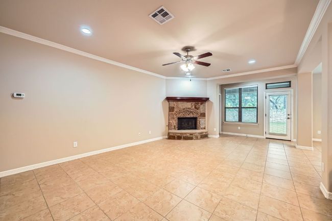 Unfurnished living room featuring a ceiling fan, light tile patterned floors, a stone fireplace, ornamental molding, and recessed lighting | Image 8