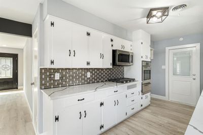 Kitchen with light hardwood / wood-style floors, tasteful backsplash, white cabinets, appliances with stainless steel finishes, and light stone countertops | Image 2