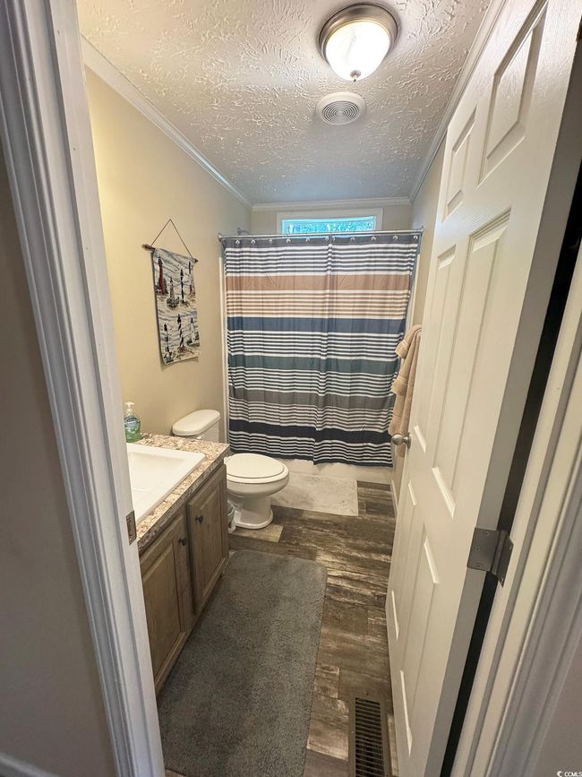 Full bath featuring a textured ceiling, wood finished floors, crown molding, vanity, and a shower with shower curtain | Image 28