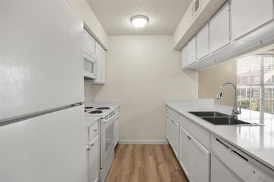 Kitchen featuring white cabinets, white appliances, a textured ceiling, light hardwood / wood-style flooring, and sink | Image 3