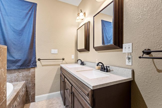 Full bath with double vanity, tiled tub, a textured wall, and a sink | Image 24
