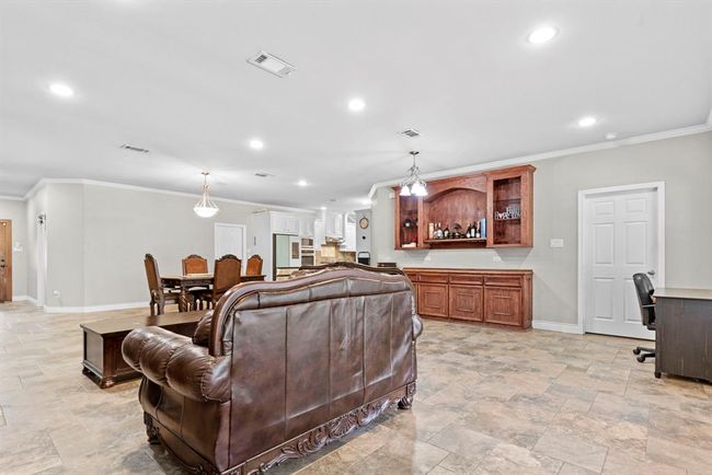 This is a spacious, open-concept living area featuring a comfortable seating space, a dining area, and a well-equipped kitchen with a bar counter. The room has tiled flooring, recessed lighting, and neutral wall colors, lending a modern and inviting atmosphere. | Image 17