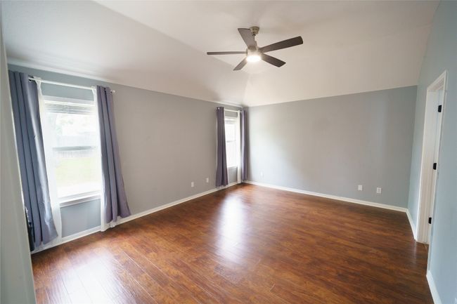 Empty room with healthy amount of natural light, a ceiling fan, wood finished floors, vaulted ceiling, and baseboards | Image 16