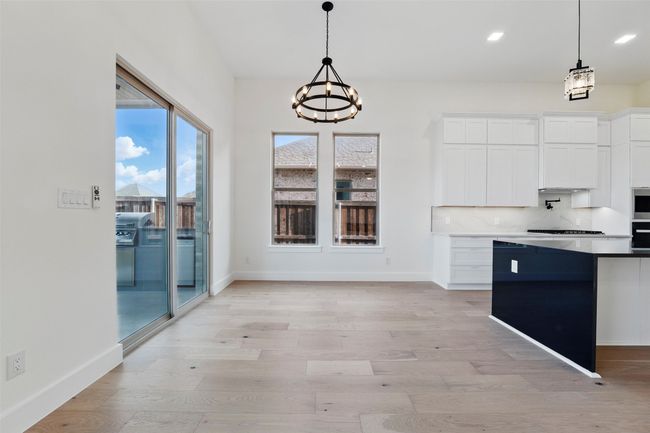 Kitchen with backsplash, black oven, white cabinets, light wood-style floors, and an inviting chandelier | Image 28