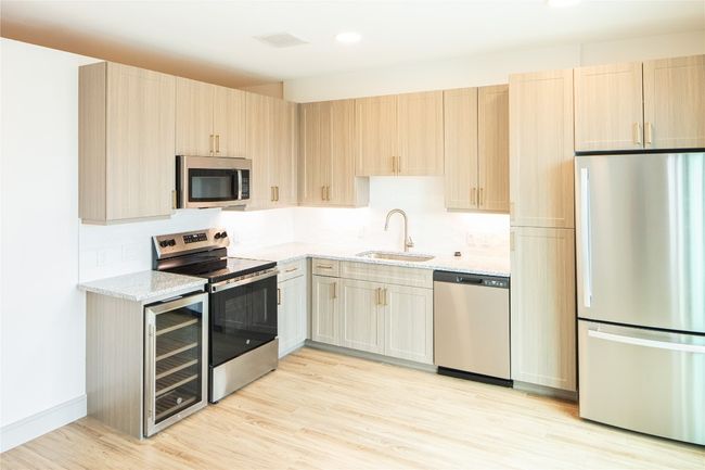 Kitchen with wine cooler, appliances with stainless steel finishes, a sink, light stone countertops, and light wood-type flooring | Image 13