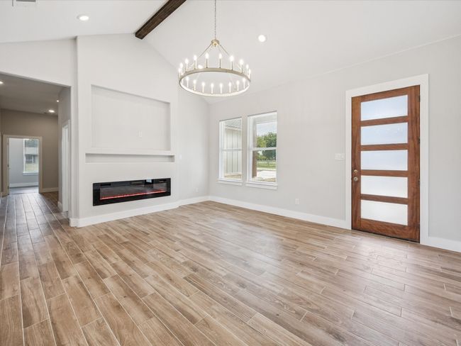 Unfurnished living room featuring a chandelier, light wood-style flooring, a glass covered fireplace, built in shelves, and recessed lighting | Image 7