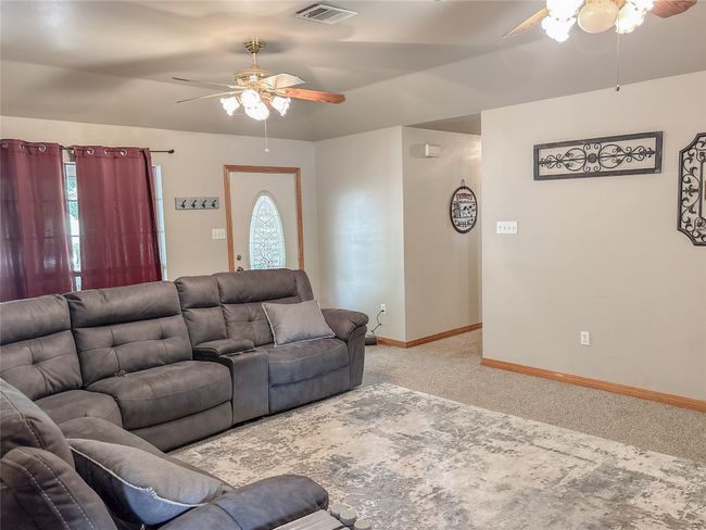 Living room with light colored carpet, visible vents, a ceiling fan, and baseboards | Image 12