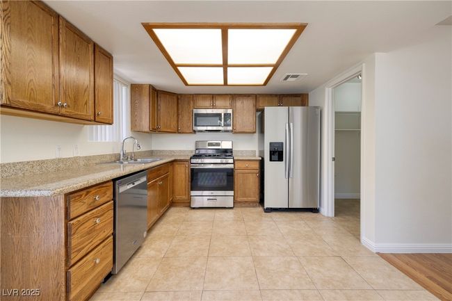 Kitchen with stainless steel appliances, brown cabinetry, and light tile patterned floors | Image 6