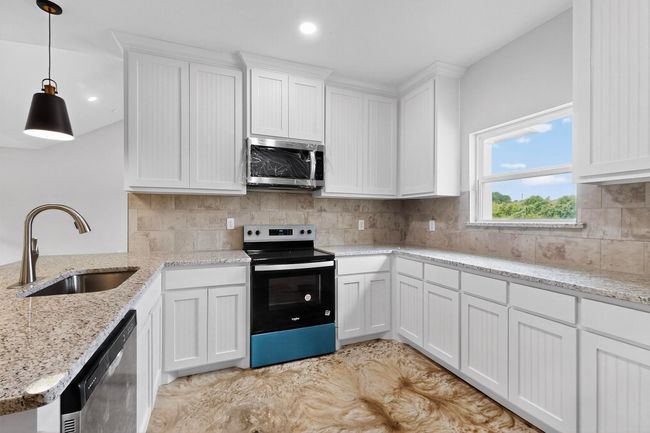 Kitchen with stainless steel appliances, white cabinets, a peninsula, backsplash, and light stone counters | Image 21