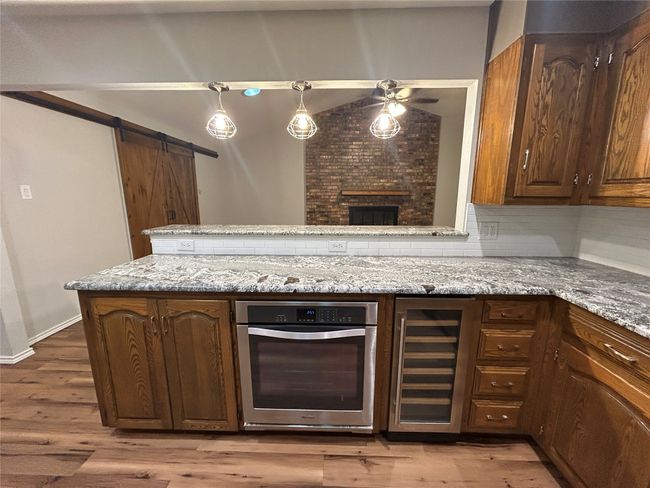 Kitchen with wine cooler, stainless steel oven, a ceiling fan, light stone countertops, and light wood finished floors | Image 17