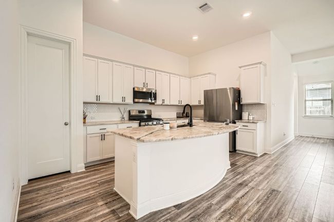 Kitchen featuring stainless steel appliances, wood finished floors, tasteful backsplash, white cabinets, and an island with sink | Image 10