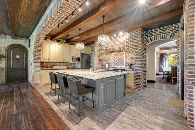 Kitchen with arched walkways, brick wall, appliances with stainless steel finishes, light wood-style floors, and cream cabinetry | Image 16
