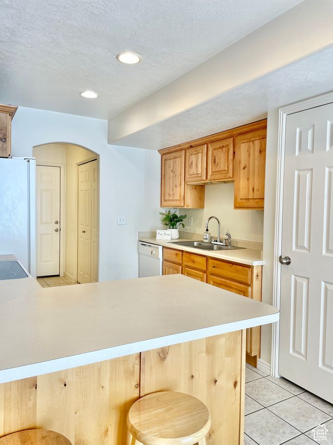 Kitchen featuring white appliances, light countertops, light tile patterned floors, a breakfast bar, and a sink | Image 9