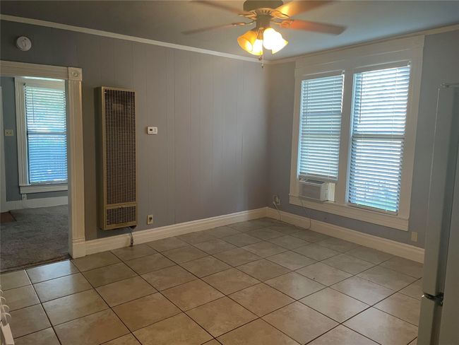 Empty room with light tile patterned floors, a heating unit, a ceiling fan, ornamental molding, and cooling unit | Image 5