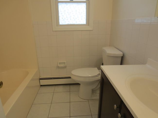 Apartment Bathroom featuring vanity, tile patterned flooring, a baseboard heating unit, tile walls, and toilet | Image 13