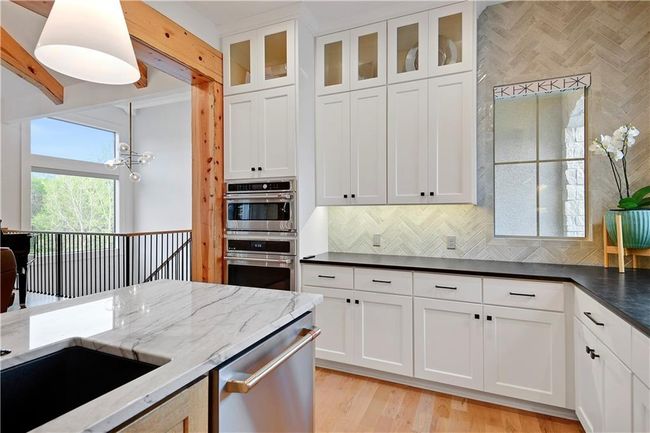 Kitchen with dark stone countertops, white cabinets, light wood-style flooring, backsplash, and appliances with stainless steel finishes | Image 20