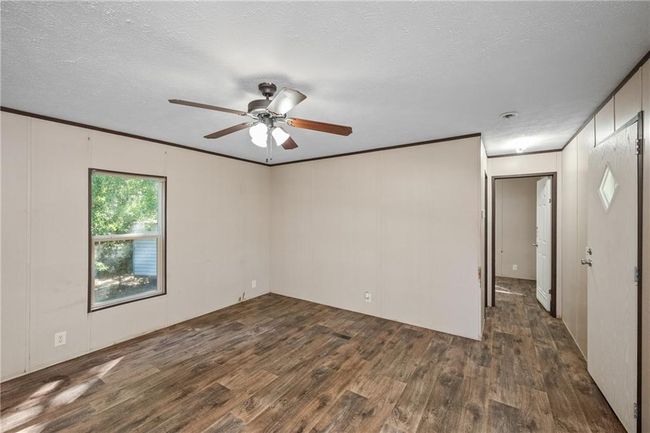 Empty room with wood finished floors, ceiling fan, crown molding, a decorative wall, and a textured ceiling | Image 13