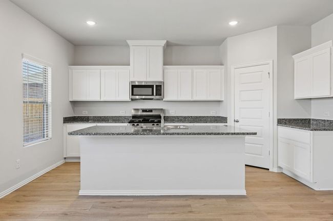 Kitchen featuring appliances with stainless steel finishes, a center island with sink, dark stone counters, white cabinetry, and recessed lighting | Image 9