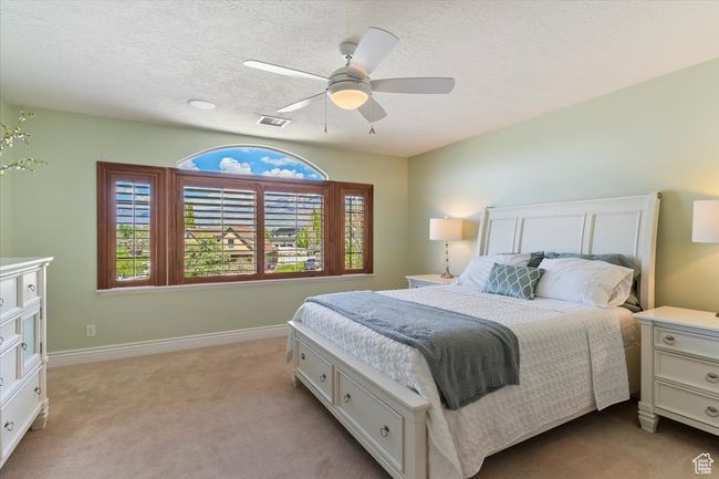 Bedroom featuring visible vents, baseboards, light colored carpet, a textured ceiling, and a ceiling fan | Image 38