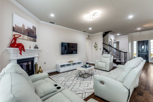 Living room with stairway, crown molding, wood finished floors, a glass covered fireplace, and recessed lighting | Image 4