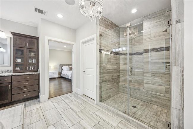 This modern bathroom features a spacious glass-enclosed shower with elegant tilework. It includes a dark wood vanity with ample storage. | Image 21