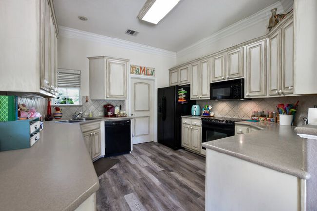 Kitchen with black appliances, cream cabinetry, crown molding, backsplash, and a peninsula | Image 10