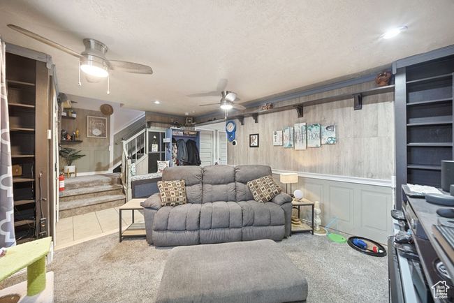 Carpeted living area with ceiling fan, tile patterned floors, stairs, a textured ceiling, and a decorative wall | Image 5