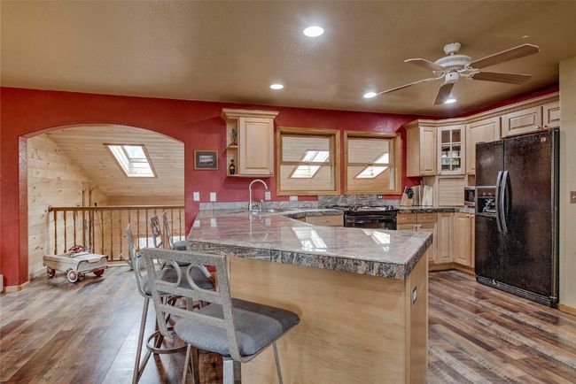 Kitchen with black fridge with ice dispenser, a breakfast bar, wood finished floors, tile counters, and a ceiling fan | Image 14