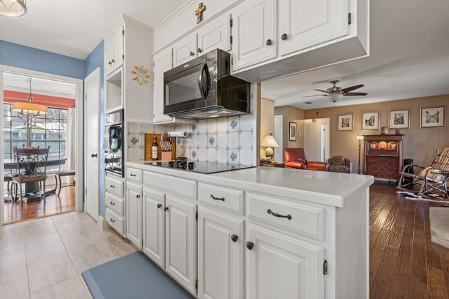 Kitchen featuring black appliances, white cabinets, decorative backsplash, ceiling fan, and decorative light fixtures | Image 14