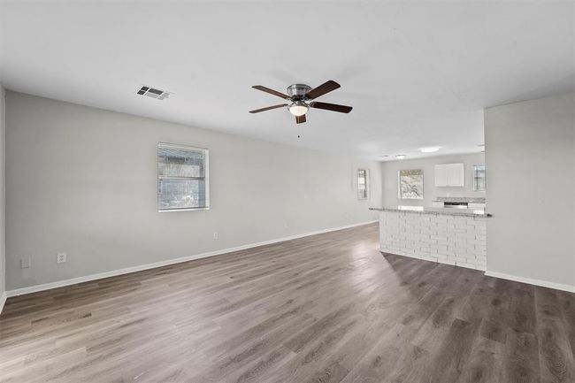 Welcome to this spacious open-concept living area with modern laminate flooring, neutral walls, and a ceiling fan. The room flows into a bright kitchen featuring a breakfast bar and ample natural light. Perfect for entertaining and family gatherings. | Image 4