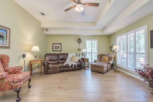 Living area featuring a raised ceiling, ceiling fan, and light wood-style tile floors | Image 25