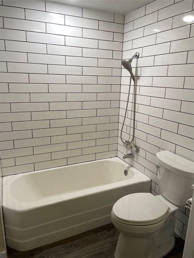 Full bath featuring toilet, wood finished floors, shower / washtub combination, and tile walls | Image 7