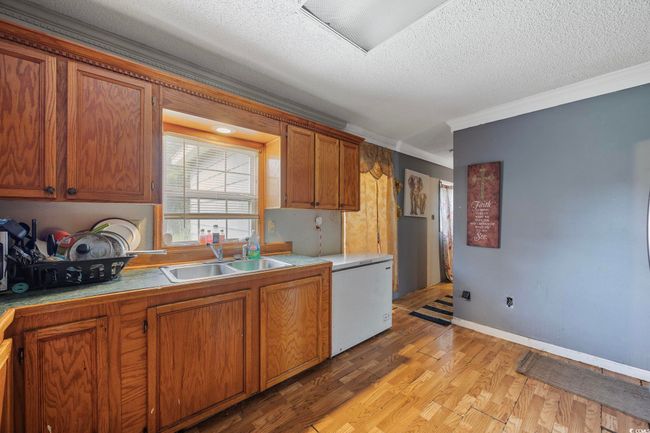 Kitchen with crown molding, light wood finished floors, brown cabinets, a textured ceiling, and light countertops | Image 11