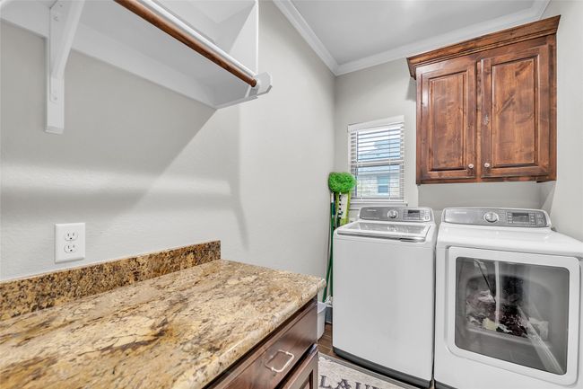 Washroom featuring washer and clothes dryer, cabinet space, ornamental molding, and wood finished floors | Image 23