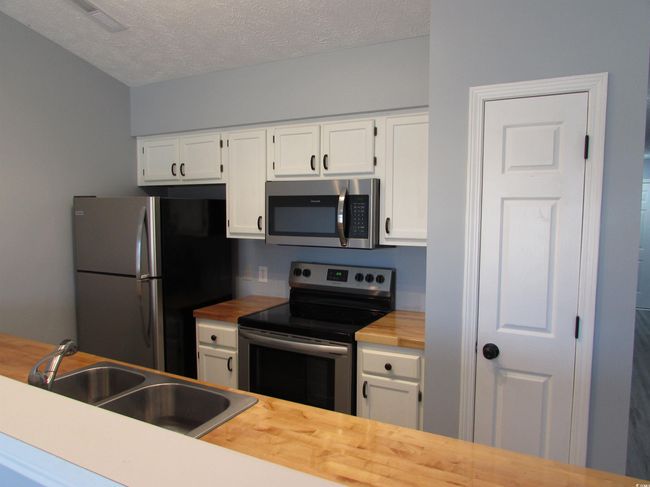 Kitchen featuring butcher block counters, white cabinetry, double bay sink and stainless steel appliances. | Image 25