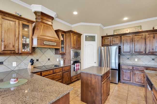 Kitchen with stainless steel appliances, stone counters, backsplash, custom range hood, and ornamental molding | Image 6