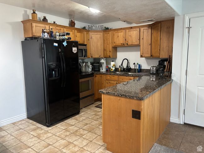 Kitchen featuring appliances with stainless steel finishes, a sink, a peninsula, brown cabinets, and a textured ceiling | Image 12