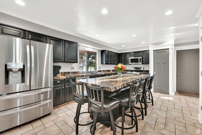 Kitchen with appliances with stainless steel finishes, dark stone countertops, a kitchen island, a breakfast bar area, and sink | Image 12