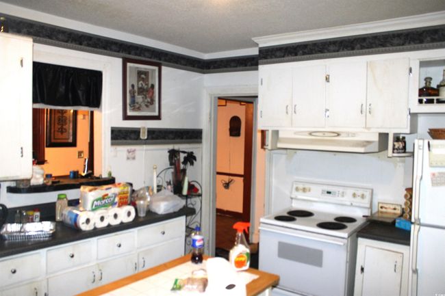 Kitchen with white appliances, ornamental molding, under cabinet range hood, white cabinetry, and dark countertops | Image 12